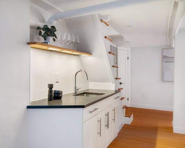 kitchen with a sink, white cabinets, light wood-style floors, open shelves, and dark countertops