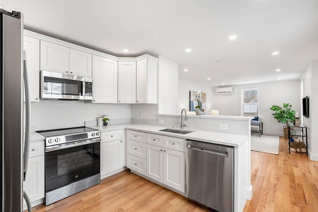 kitchen with white cabinets, appliances with stainless steel finishes, a peninsula, light countertops, and a sink