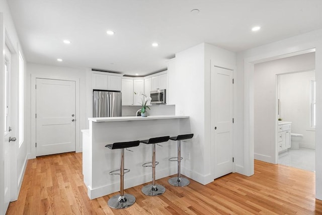 kitchen with light countertops, appliances with stainless steel finishes, light wood-style floors, white cabinets, and a peninsula