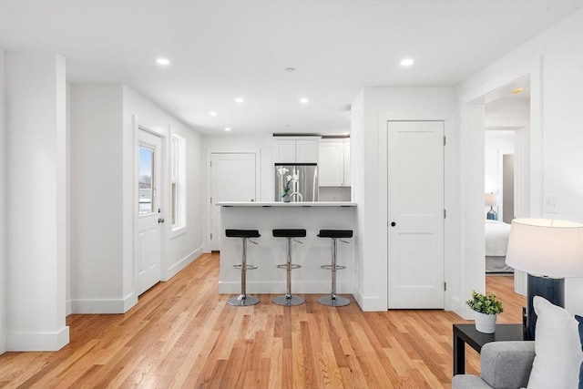 interior space with light wood-style flooring, recessed lighting, white cabinetry, a kitchen breakfast bar, and stainless steel refrigerator