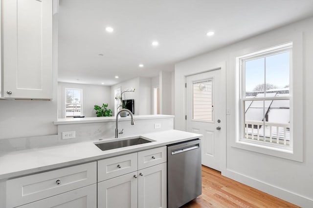 kitchen with light countertops, stainless steel dishwasher, light wood-style floors, white cabinets, and a sink