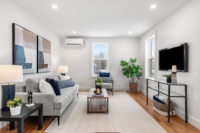 living room featuring a wall unit AC, light wood finished floors, baseboards, and recessed lighting