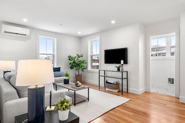 living room with a healthy amount of sunlight, light wood-style floors, recessed lighting, and a wall mounted AC