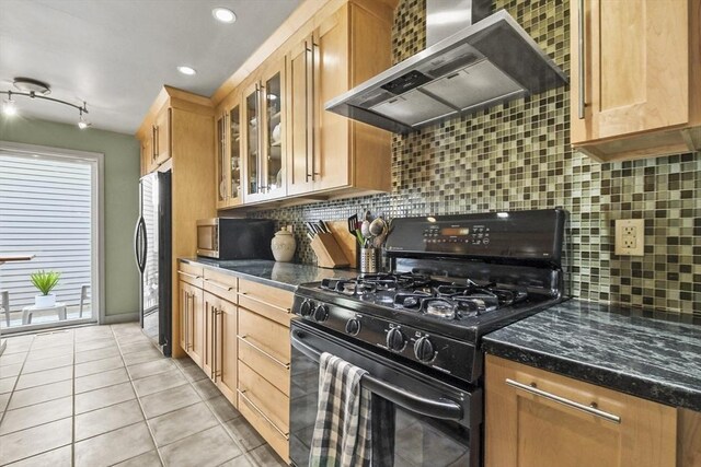 kitchen with light tile patterned flooring, backsplash, wall chimney range hood, appliances with stainless steel finishes, and dark stone counters