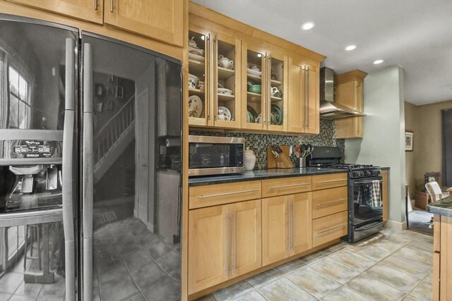 kitchen featuring light tile patterned floors, backsplash, wall chimney range hood, black appliances, and dark stone countertops