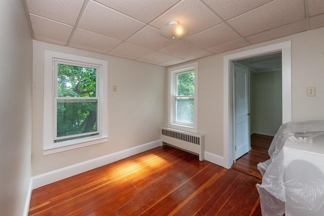 empty room featuring dark wood-type flooring, radiator, a paneled ceiling, and baseboards