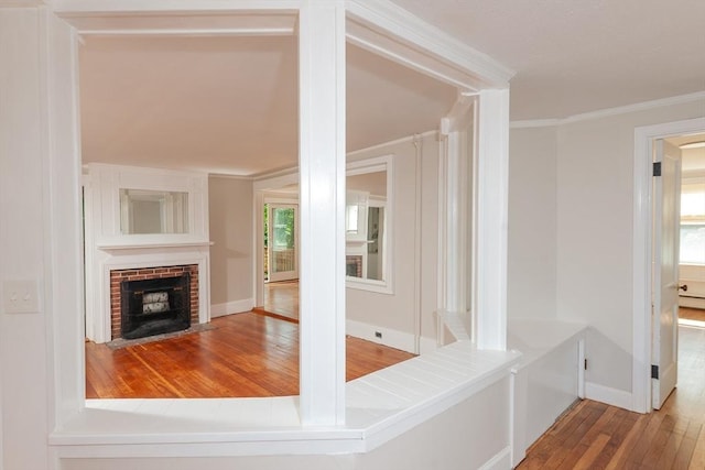 interior space featuring baseboards, a brick fireplace, wood finished floors, and crown molding