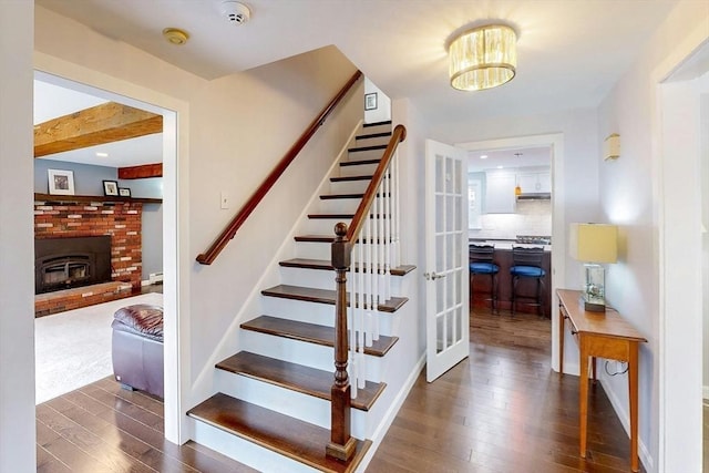 stairway with wood finished floors, a fireplace, baseboards, baseboard heating, and a notable chandelier