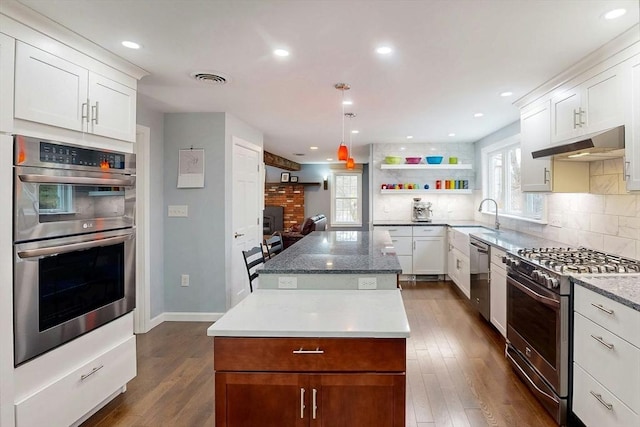 kitchen featuring decorative backsplash, a center island, under cabinet range hood, a sink, and appliances with stainless steel finishes