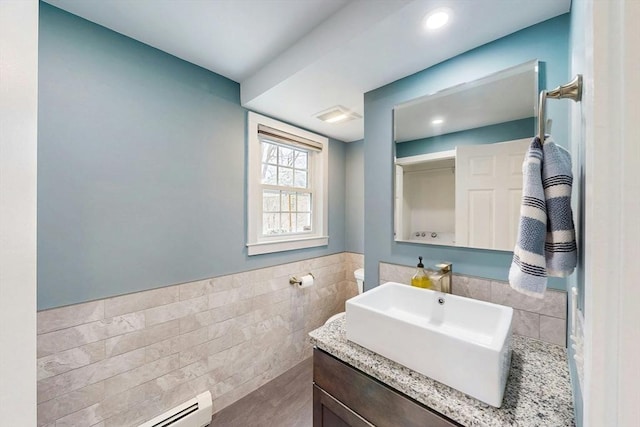 bathroom featuring tile walls, wainscoting, vanity, a baseboard radiator, and recessed lighting
