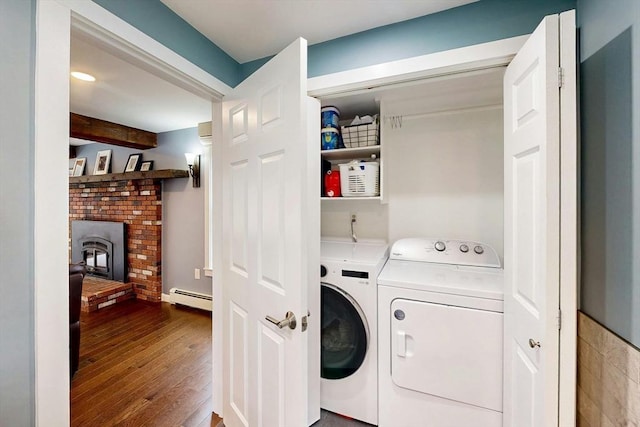 laundry area featuring laundry area, a fireplace, washing machine and dryer, a baseboard radiator, and hardwood / wood-style floors