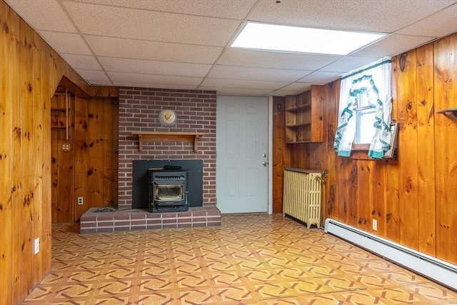 224 Palmer Rd, Monson, MA 01057 - unfurnished living room with baseboard heating, wood walls, a wood stove, light floors, and a paneled ceiling