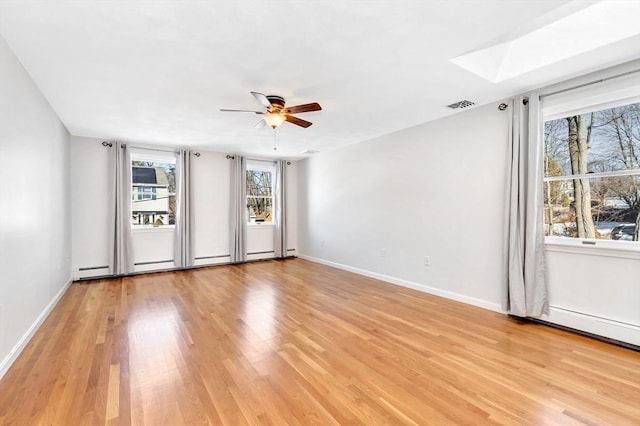 unfurnished room with ceiling fan, a skylight, and light hardwood / wood-style floors