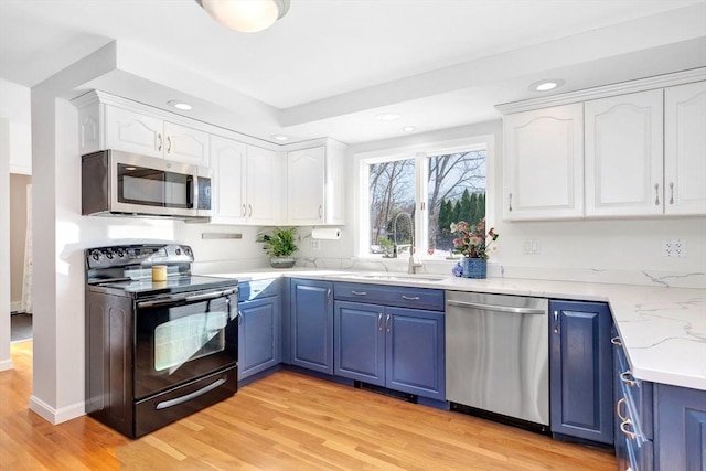 kitchen featuring light wood-type flooring, blue cabinetry, white cabinetry, appliances with stainless steel finishes, and sink