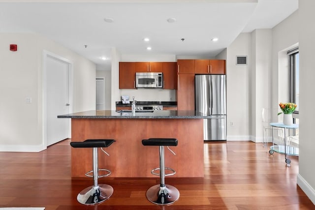 kitchen with appliances with stainless steel finishes, a breakfast bar, hardwood / wood-style floors, sink, and a center island with sink