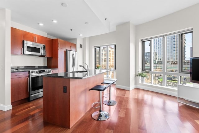 kitchen with sink, dark wood-type flooring, a kitchen breakfast bar, stainless steel appliances, and an island with sink