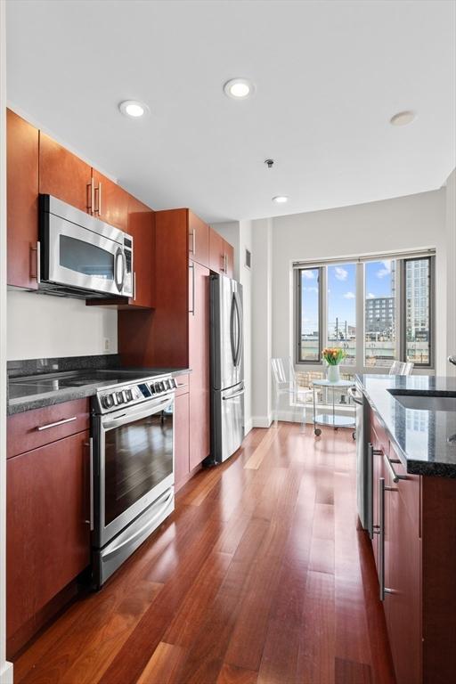 kitchen featuring dark wood-type flooring, stainless steel appliances, sink, and dark stone countertops