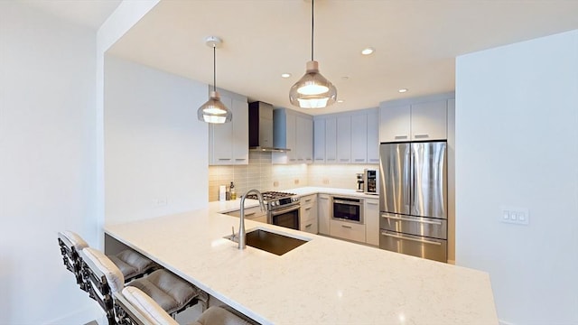 kitchen featuring stainless steel appliances, wall chimney exhaust hood, decorative backsplash, a peninsula, and a sink