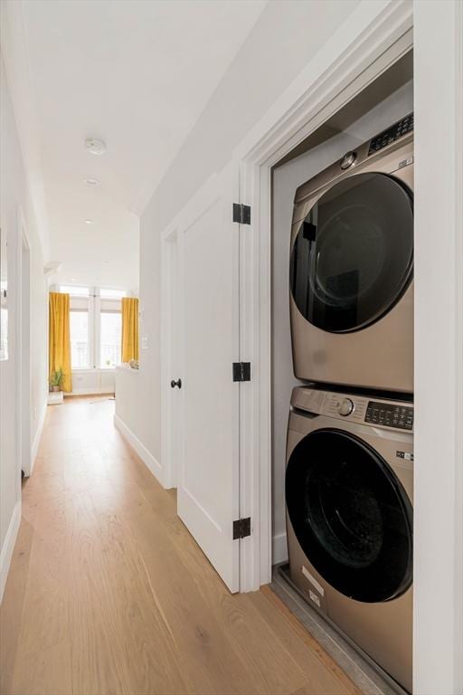 laundry area with light wood-style floors, stacked washer and clothes dryer, baseboards, and laundry area