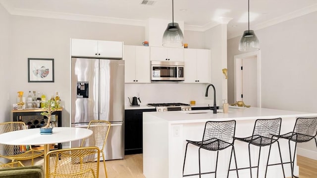 kitchen featuring crown molding, light wood finished floors, appliances with stainless steel finishes, a sink, and a kitchen breakfast bar