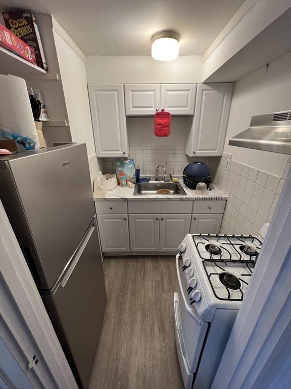 kitchen with a sink, freestanding refrigerator, wall chimney exhaust hood, white range with gas cooktop, and dark wood finished floors