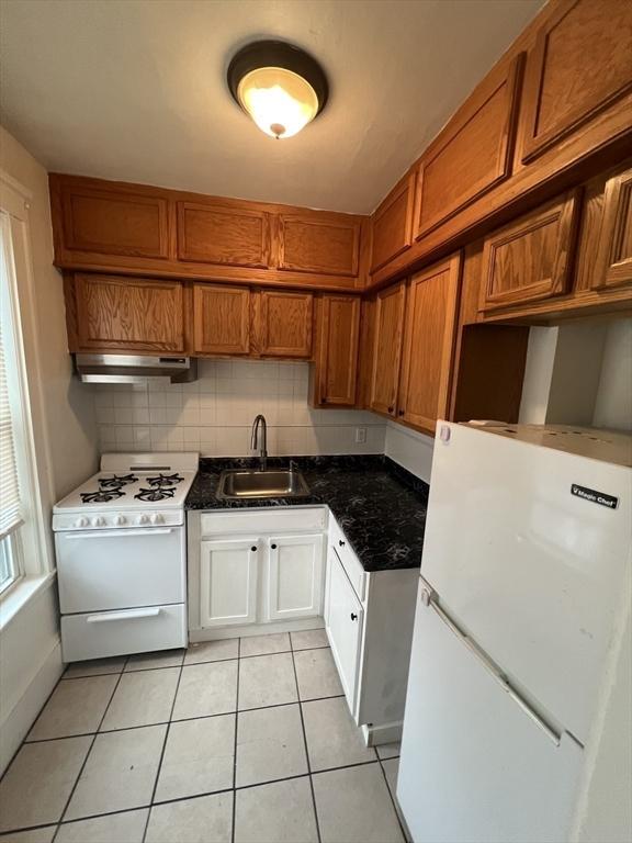 kitchen featuring light tile patterned floors, a sink, dark countertops, white appliances, and under cabinet range hood