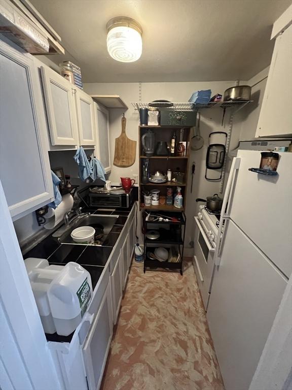 kitchen with a sink, freestanding refrigerator, white cabinetry, and range with gas stovetop