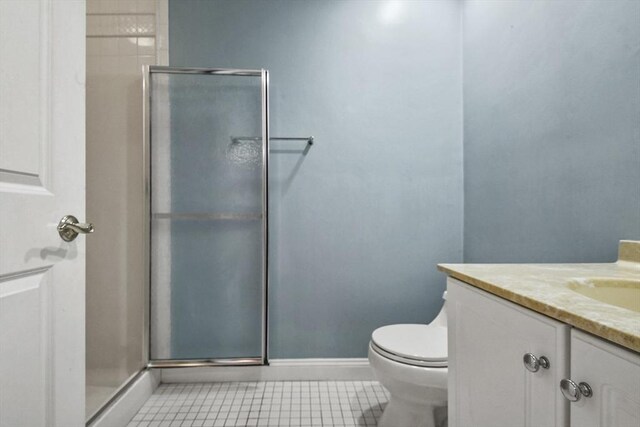 bathroom featuring tile patterned flooring, vanity, toilet, and a shower with door