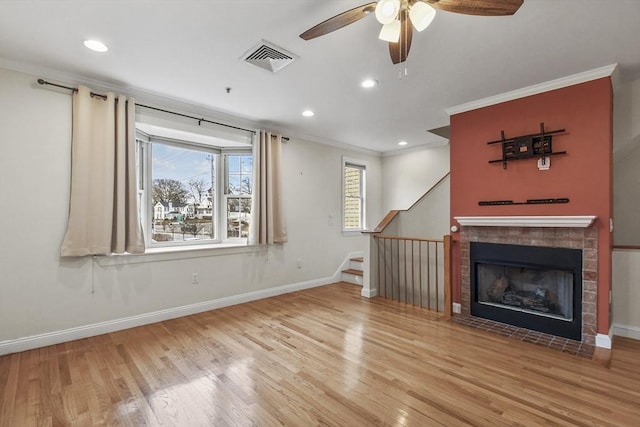 unfurnished living room with hardwood / wood-style flooring, ceiling fan, crown molding, and a tiled fireplace