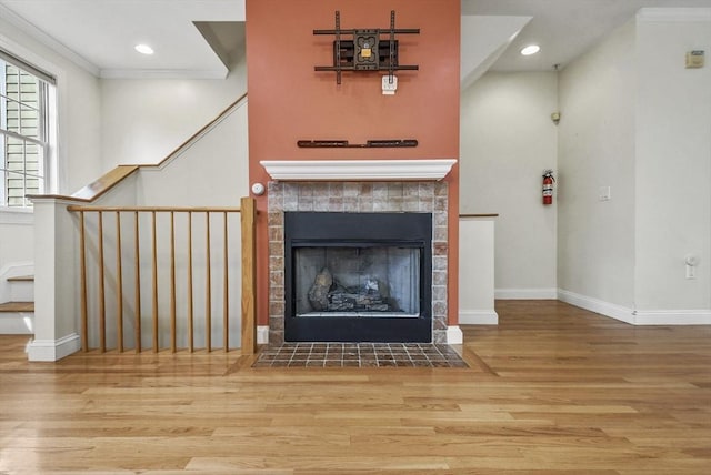 unfurnished living room featuring wood-type flooring, ornamental molding, and a tiled fireplace