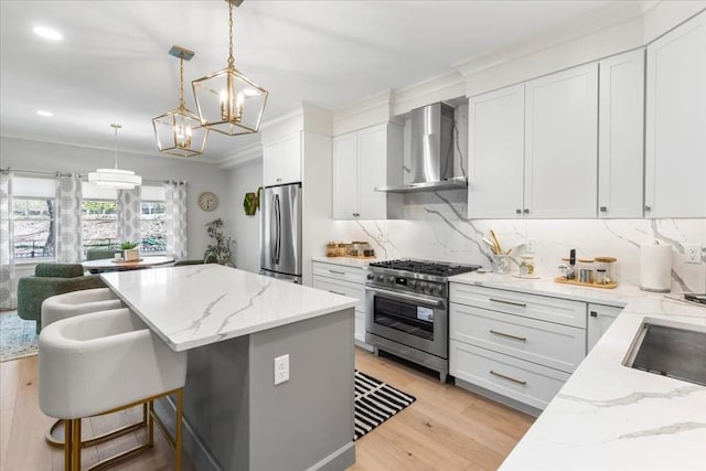 kitchen featuring appliances with stainless steel finishes, a center island, light stone counters, white cabinets, and wall chimney exhaust hood