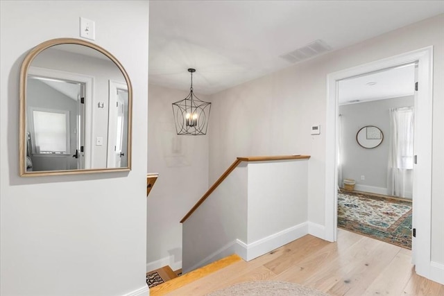 corridor featuring visible vents, wood finished floors, baseboards, a chandelier, and an upstairs landing