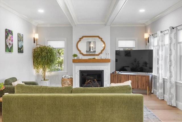 living area with a fireplace, beamed ceiling, ornamental molding, and light wood-type flooring