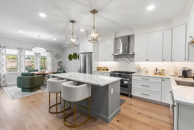 kitchen with wall chimney range hood, crown molding, appliances with stainless steel finishes, a center island, and recessed lighting