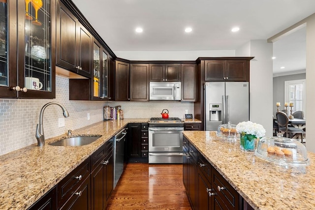 kitchen featuring stainless steel appliances, a sink, dark brown cabinets, light stone counters, and recessed lighting
