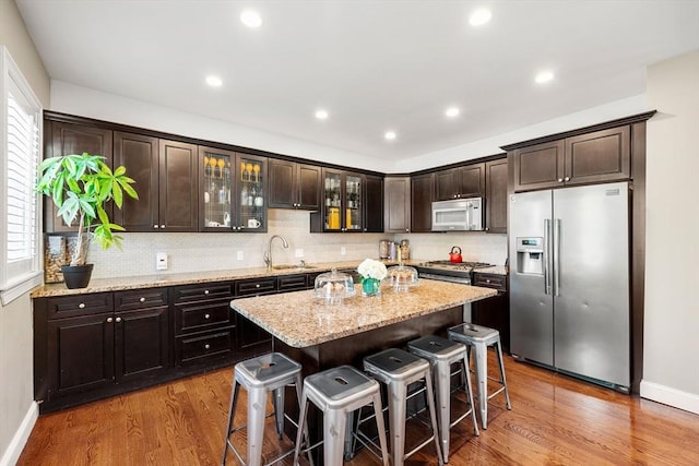 kitchen with stainless steel appliances, a sink, a kitchen bar, baseboards, and wood finished floors