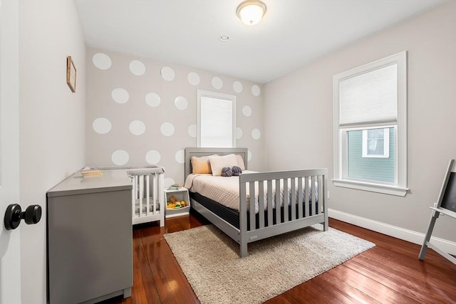 bedroom with baseboards, an accent wall, wallpapered walls, wood finished floors, and radiator heating unit