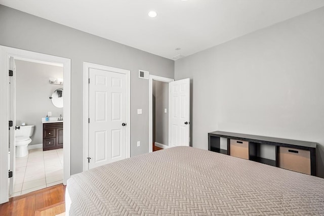 bedroom with ensuite bathroom, a sink, wood finished floors, and recessed lighting