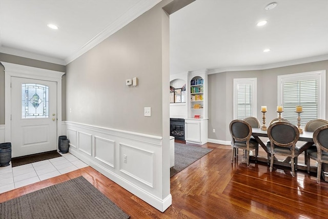 foyer entrance featuring a glass covered fireplace, crown molding, wood finished floors, recessed lighting, and a wainscoted wall