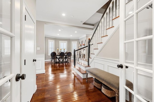 foyer entrance featuring stairway, crown molding, wood-type flooring, a decorative wall, and a wainscoted wall