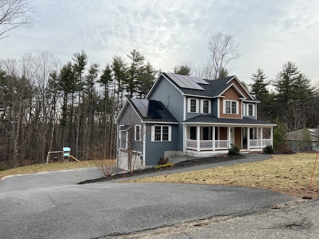 view of front facade featuring a porch, a garage, solar panels, and a front yard