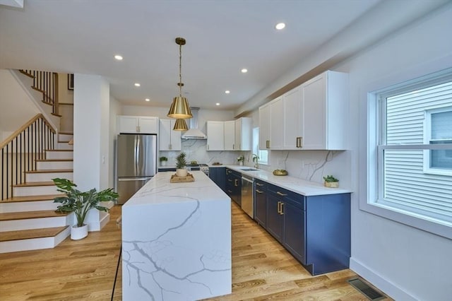 18 Belknap St Unit 2, Arlington, MA 02474 - kitchen with appliances with stainless steel finishes, blue cabinets, wall chimney range hood, white cabinetry, and backsplash