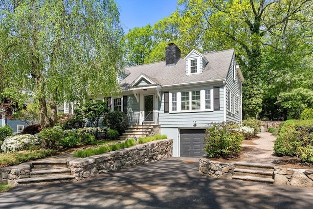 new england style home featuring asphalt driveway, a garage, a chimney, and a shingled roof