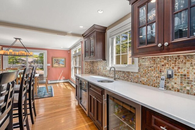 bar featuring a sink, decorative backsplash, light wood-type flooring, baseboard heating, and beverage cooler