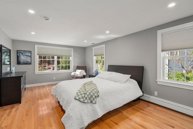 bedroom featuring multiple windows, light wood finished floors, baseboard heating, recessed lighting, and baseboards