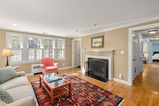 living room featuring radiator, a fireplace with flush hearth, crown molding, wood finished floors, and baseboards