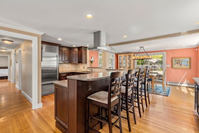 kitchen with built in refrigerator, island exhaust hood, baseboards, a kitchen breakfast bar, and light wood-style floors