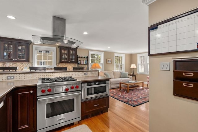 kitchen featuring stainless steel appliances, island range hood, light wood finished floors, backsplash, and recessed lighting