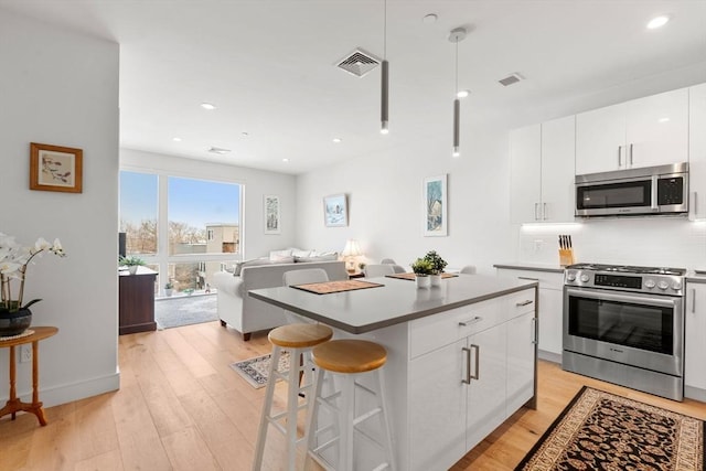 kitchen with a kitchen island, appliances with stainless steel finishes, a breakfast bar, white cabinetry, and light wood-type flooring