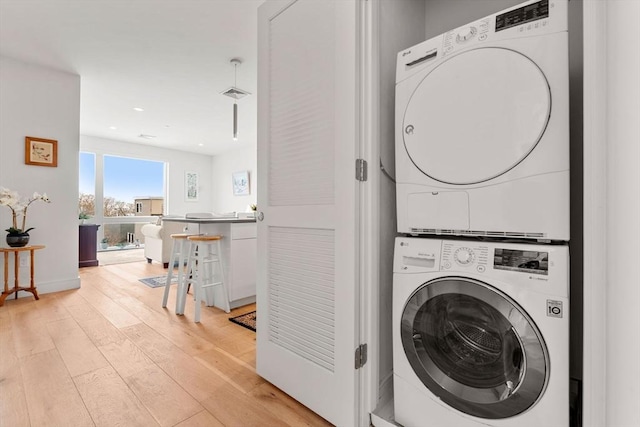 washroom with stacked washer / drying machine and light hardwood / wood-style floors